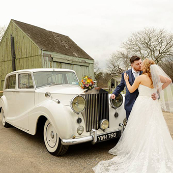 Bride and groom kiss in front of a Rolls Royce Silver Wraith.